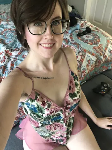 Smiling woman in floral lace camisole relaxing on a patterned bed in a cozy bedroom setting.