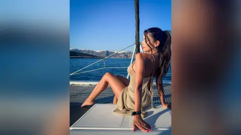 Woman in a gold backless dress relaxing on a boat deck under a clear blue sky during a summer sunset.