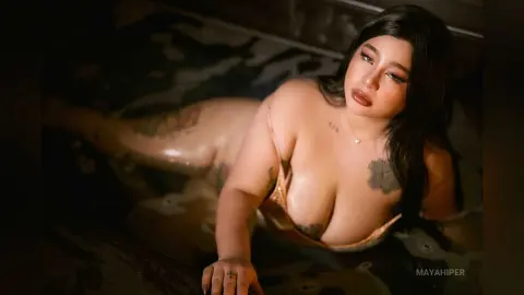 Curvy woman in a gold bikini relaxing in a dark, moody outdoor pool with tattoos.