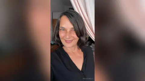 MichaelaBelle smiles while wearing a black button-down shirt with her dark hair styled in a shoulder-length bob.
