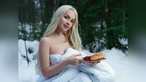 EllieFrosty poses in a snowy forest, wrapped in a white quilted blanket while holding a plate of raspberries and a pastry.