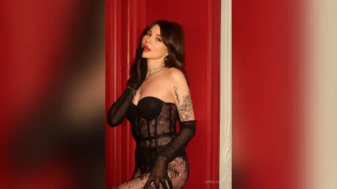 Glamorous woman in a black lace corset and sheer gloves posing against a bold red background.