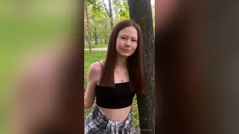 Young woman in a black crop top and plaid shirt relaxing in a lush green forest setting.