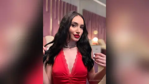 Glamorous woman with long dark hair in a red satin v-neck dress posing in a soft-lit luxury room.