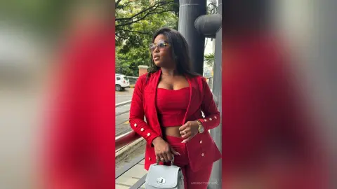 Stylish woman in a bold red suit and sunglasses posing confidently outdoors in a city setting.