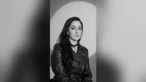 Stylish woman in a black leather jacket and choker posing for a moody black and white studio portrait.