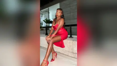 Stylish woman in a red cocktail dress and red heels sitting outdoors at night.