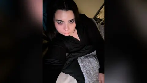 Young woman with dark hair wearing a black long-sleeve top relaxing in a cozy indoor setting.