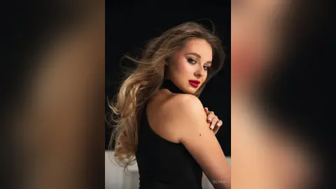 Elegant woman with flowing blonde hair in a black sleeveless top posing against a dark studio background.