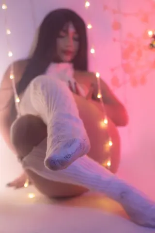 ShaniaDaniel — Woman in white knit thigh-high socks sitting in a dreamy room with warm fairy lights.