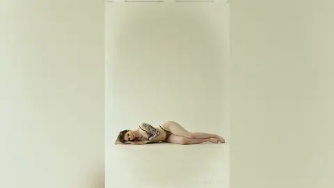 Young woman in a patterned bikini relaxing on a white studio floor in a minimalist, serene setting.
