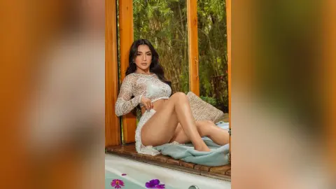 Beautiful woman in a white lace crochet outfit relaxing on a wooden deck in a lush tropical garden setting.