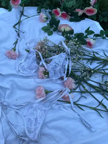 White lace lingerie set scattered with pink roses on a white fabric background for a romantic aesthetic.