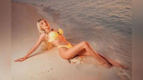 Blonde woman in a yellow bikini relaxing on a tropical beach at sunset.