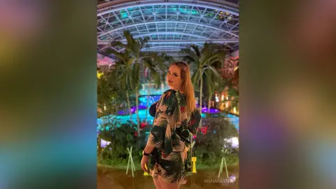 Young woman in a tropical print dress posing in a lush indoor botanical garden at night.