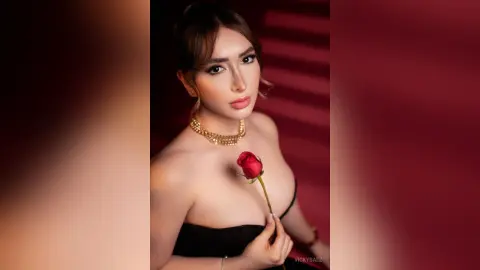 Elegant woman in a black strapless dress holding a red rose against a romantic red background.