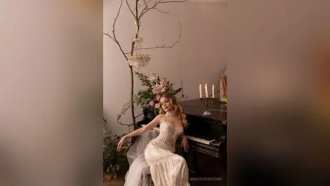 Elegant woman in a white lace gown leaning against a grand piano in a dreamy, ethereal indoor setting.