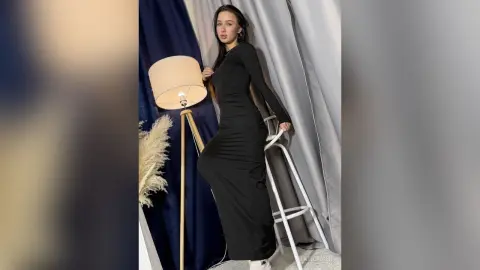 Elegant woman in a sleek black maxi dress posing in a studio setting with soft lighting.