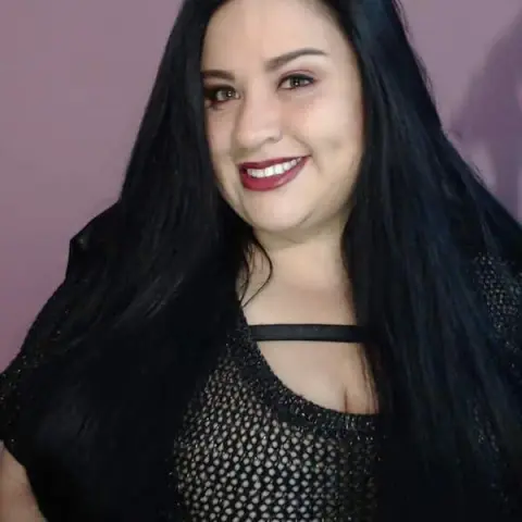 Smiling woman with long black hair wearing a black mesh top against a purple background.