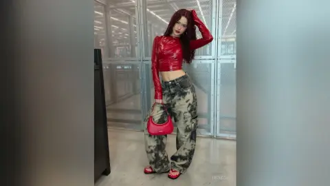 Stylish woman in a red long-sleeve crop top and tie-dye cargo pants posing in a modern industrial hallway.