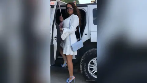 Stylish woman in a white mini dress and blue heels stepping out of a white vehicle on a sunny day.