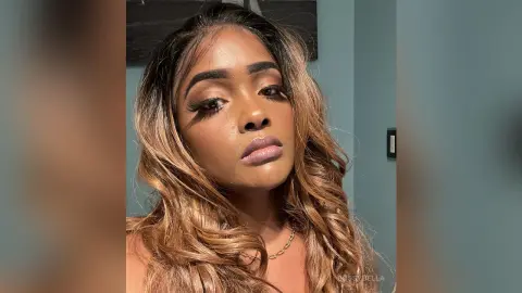 BossyBella — BossyBella poses with long, wavy brown hair and heavy eye makeup, looking directly at the camera in a close-up headshot.