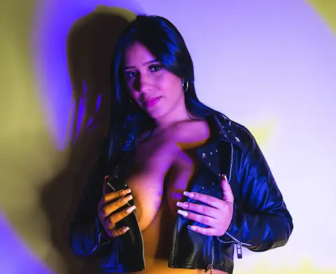 Young woman in a black leather jacket posing under moody blue and yellow studio lighting.