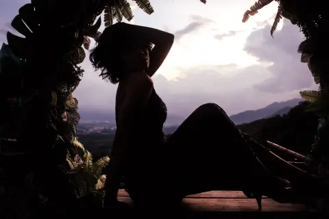 Raven_Morningstar sits in silhouette wearing a wide-brimmed hat against a sunset mountain backdrop.