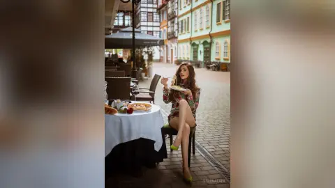 Elegant woman in a floral dress enjoying a meal at an outdoor cafe in a charming European cobblestone street.