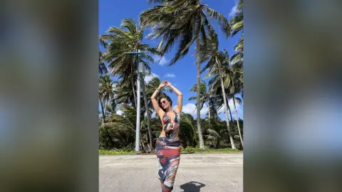 Stylish woman in a patterned cutout maxi dress posing under palm trees on a sunny tropical beach day.
