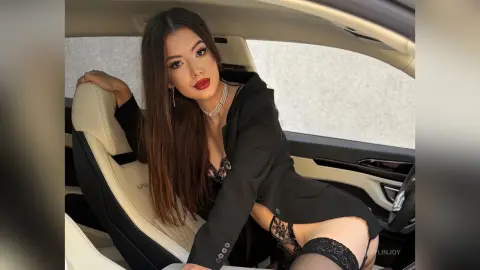 Glamorous woman in a black blazer and lace lingerie sitting in a luxury car interior with a confident mood.