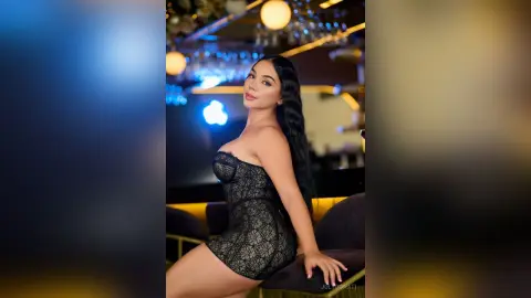 Glamorous woman in a black lace corset dress posing in a moody, dimly lit upscale lounge setting.