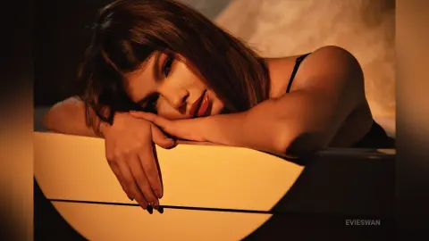 Young woman in a black tank top leaning on a white surface in warm, moody indoor lighting.