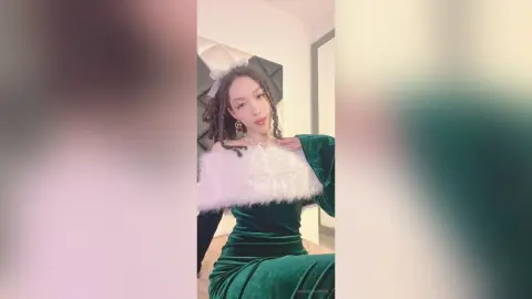 Young woman in a glamorous dark green velvet dress with white faux fur trim posing in a bright room.