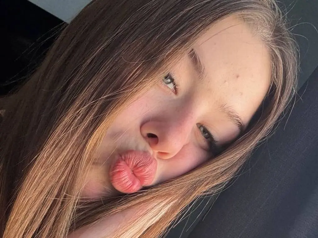Close-up selfie of a young woman with long brown hair making a playful pouty face in a car.