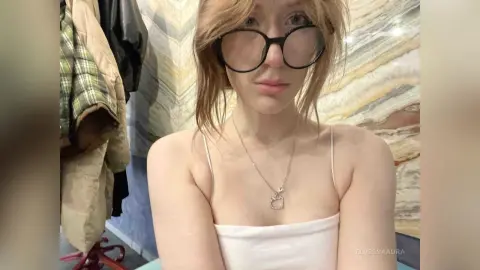 Young woman with glasses and a white camisole posing in a modern room with marble walls.