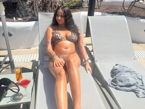 JasmineDesire22 wearing a leopard print bikini while sitting on a grey lounge chair outdoors in the sun.