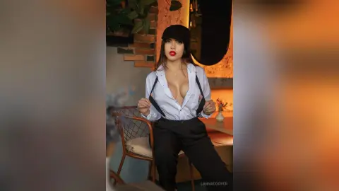 Young woman in a white button-down shirt and black trousers posing confidently in a cozy indoor setting.