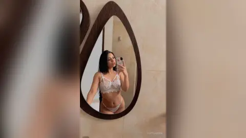 Young woman in white lace lingerie taking a selfie in a modern bathroom mirror.