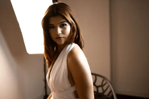 Elegant woman in a white sleeveless dress posing in soft studio lighting for a moody portrait.