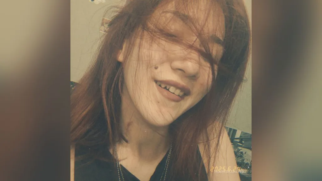 Close-up portrait of a young woman with red hair posing against a floral pattern background in warm red lighting.
