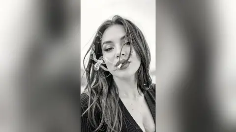 Moody black and white portrait of a young woman with long hair smoking a cigarette outdoors.
