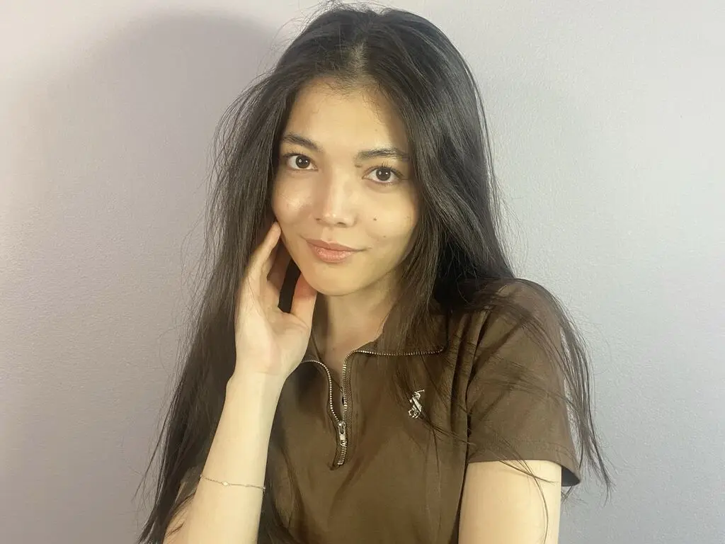 Smiling young woman with long dark hair wearing a brown polo shirt against a neutral grey wall.