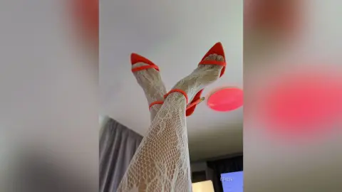 Low angle view of a woman wearing white lace tights and bright orange high heel sandals in a bright room.