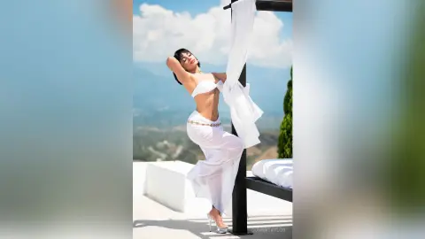 Elegant woman in a white summer outfit posing on a sunny luxury terrace overlooking a scenic mountain view.
