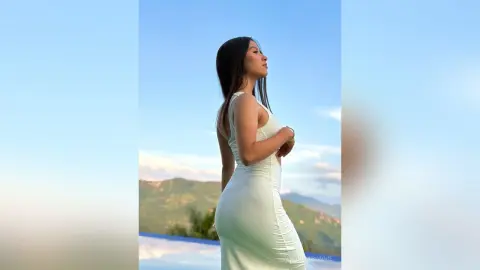 Elegant woman in a white bodycon dress posing against a scenic mountain landscape under a clear blue sky.