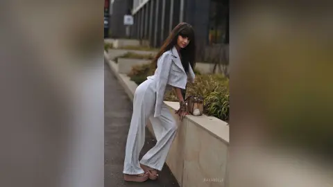 Stylish woman in a white linen suit posing elegantly by a stone planter in an urban outdoor setting.