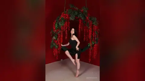 Woman in a black dress posing under a lush red floral arch against a deep red background.