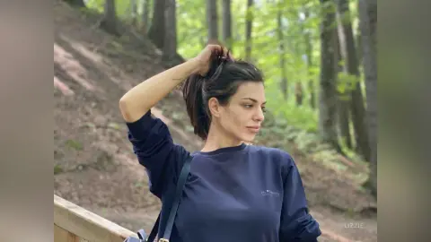 Young woman in a navy blue sweatshirt relaxing in a lush, sunlit forest setting.