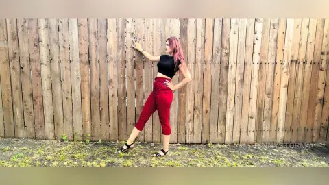 Stylish woman in a black crop top and red trousers posing confidently against a rustic wooden fence.